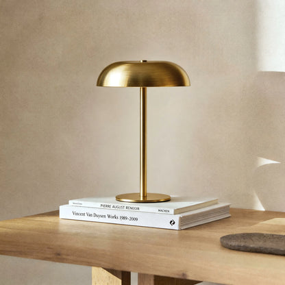 Brass-finished cordless mushroom table lamp resting on a wooden desk, showcasing its sleek metallic texture and architectural design.
