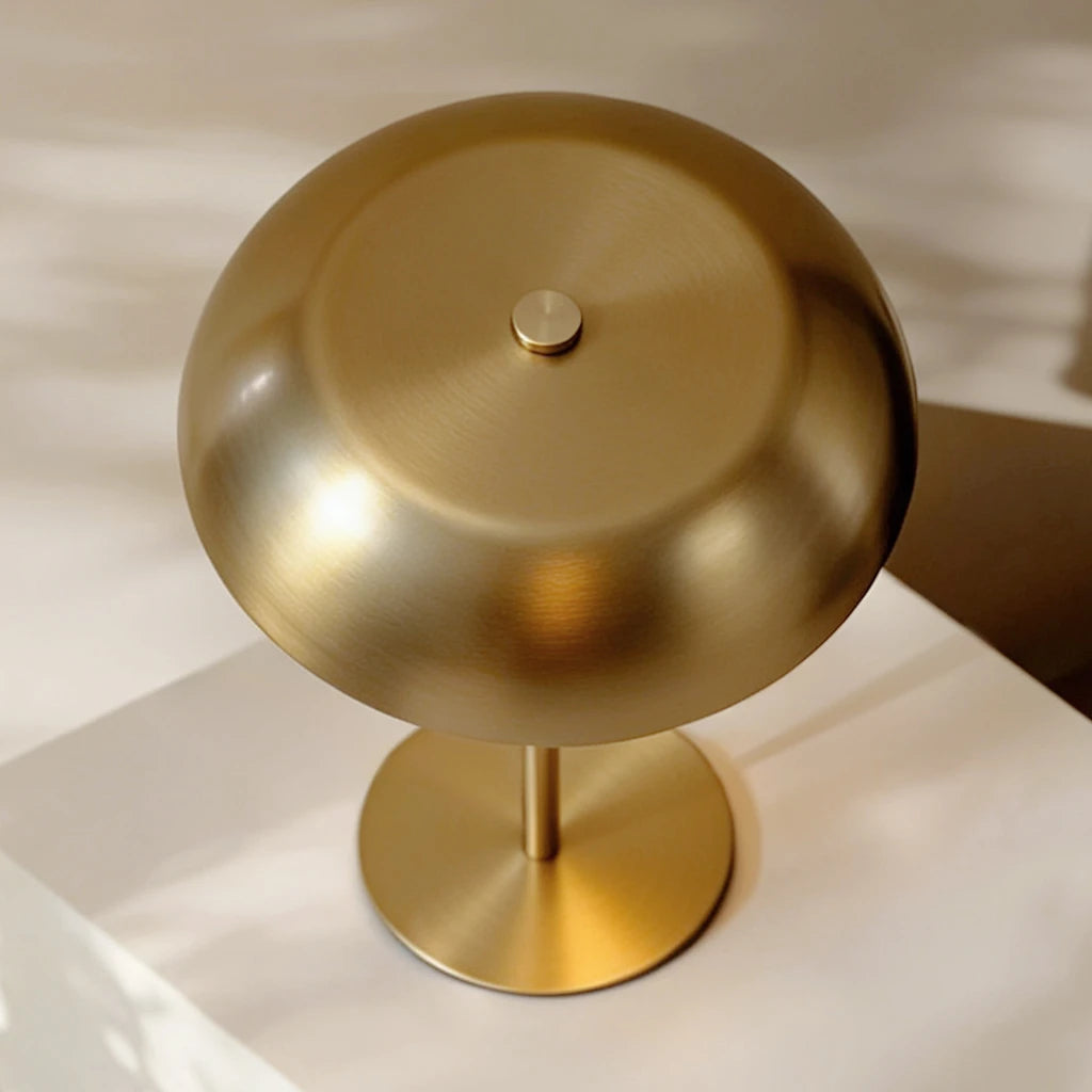 Detail view of the hand-polished brushed brass texture on the mushroom-shaped dome and cylindrical stem of the cordless table lamp.